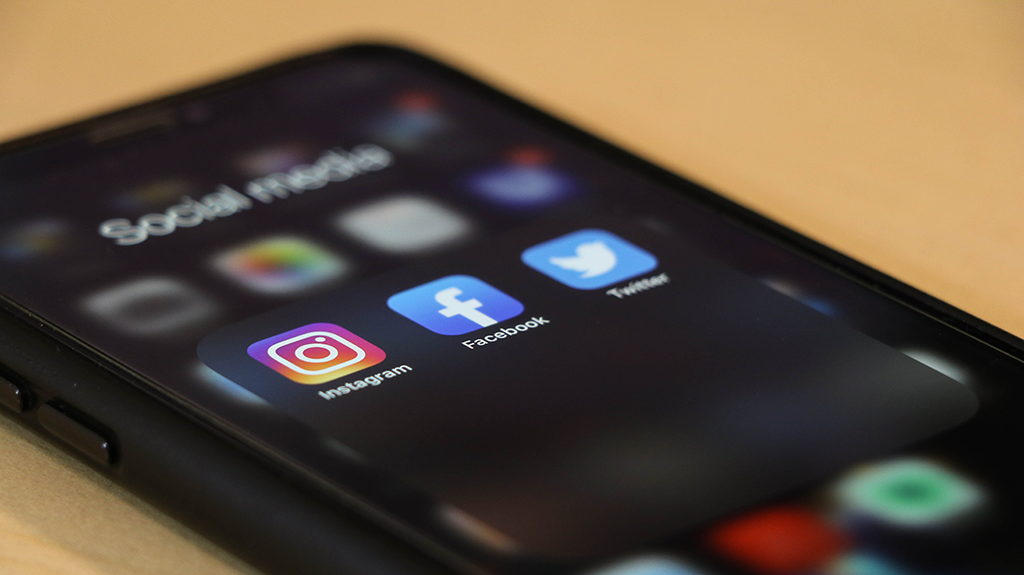 iphone with social media folder open displaying instagram, facebook and twitter apps - Dragon360