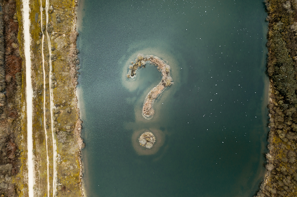 aerial drone shot of question mark island in body of water - Dragon360