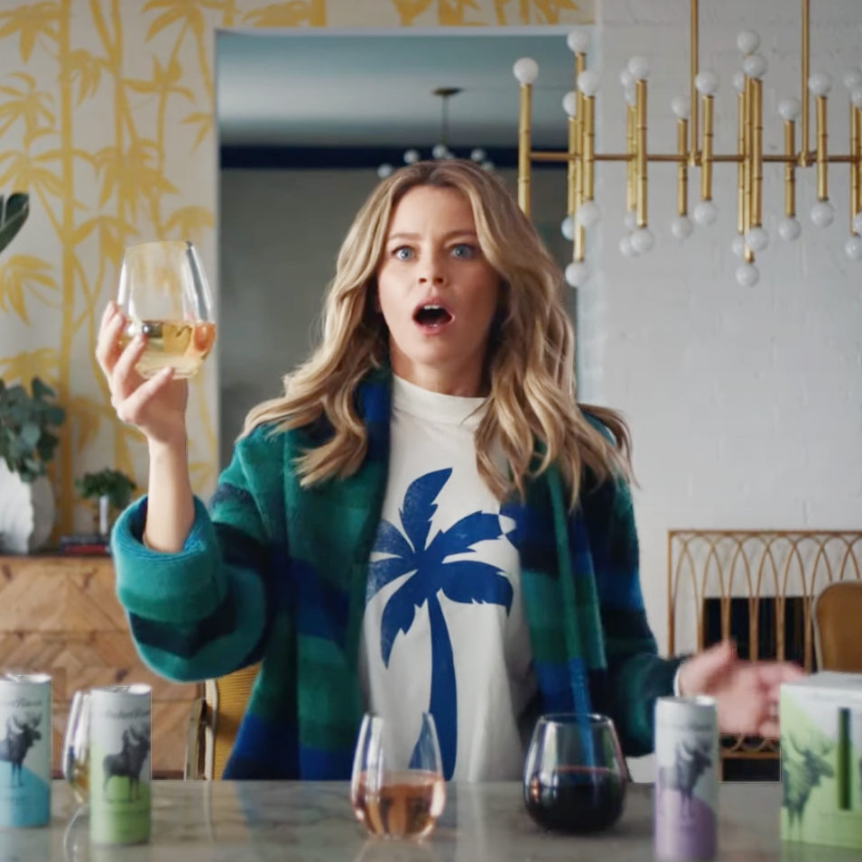 elizabeth banks in a blue palm tree tshirt holding a glass of archer roose rosé